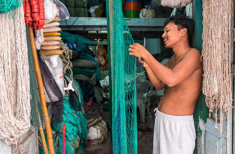 Merchant in the streets of Yangon webbing a fishing net in his storefront