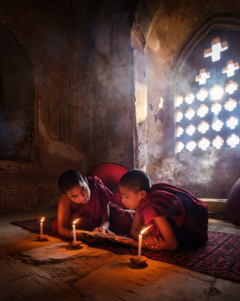 Monks inside a temple reading a book around candlelight on a temple in Bagan.