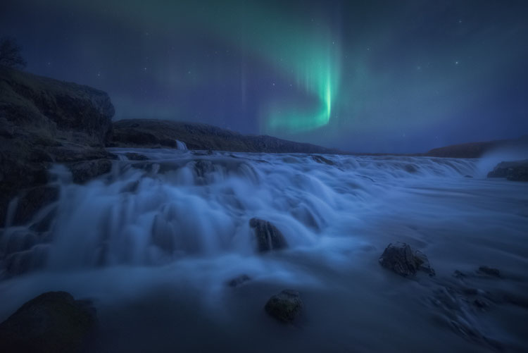 long exposure creates a moving aurora over running water over a waterfall