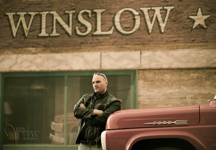 Man standing on the corner at Winslow Arizona, leaning up against a flat bed ford