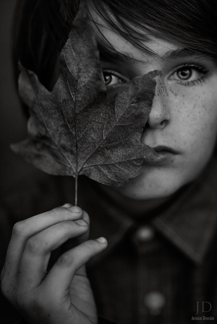 black and white portrait of a small boy holding a leaf in front of his face