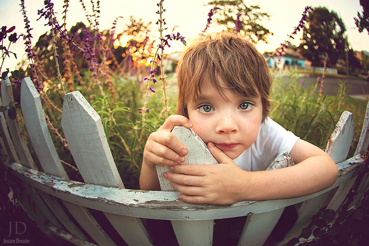 close up photo with a wide angle lens of my kid leaning on a white picket fence