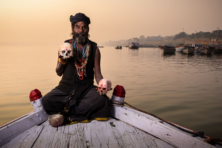 An Aghori Sadhu sits on a boat on the water in India showing original photo