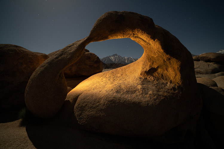 night photo of same stone arch but with a small light source illuminating it for effect