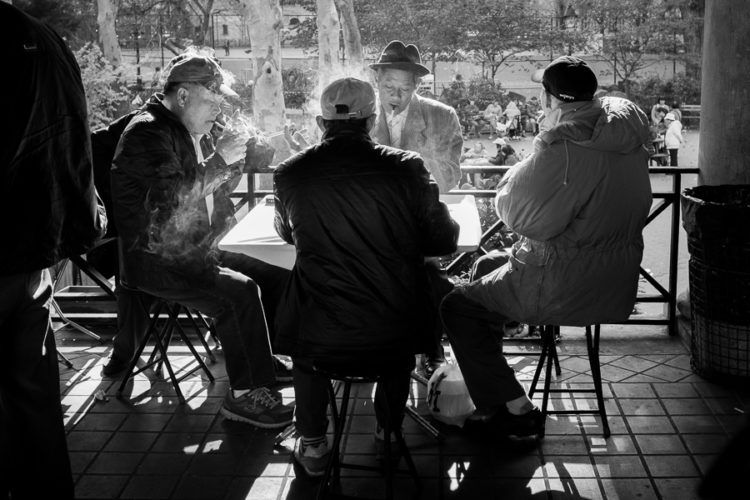 men sit at a table smoking while they watch the activities outside