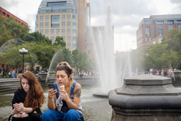 street photography shot of two girls on their mobile phones while sitting at a fountain during a recent trip