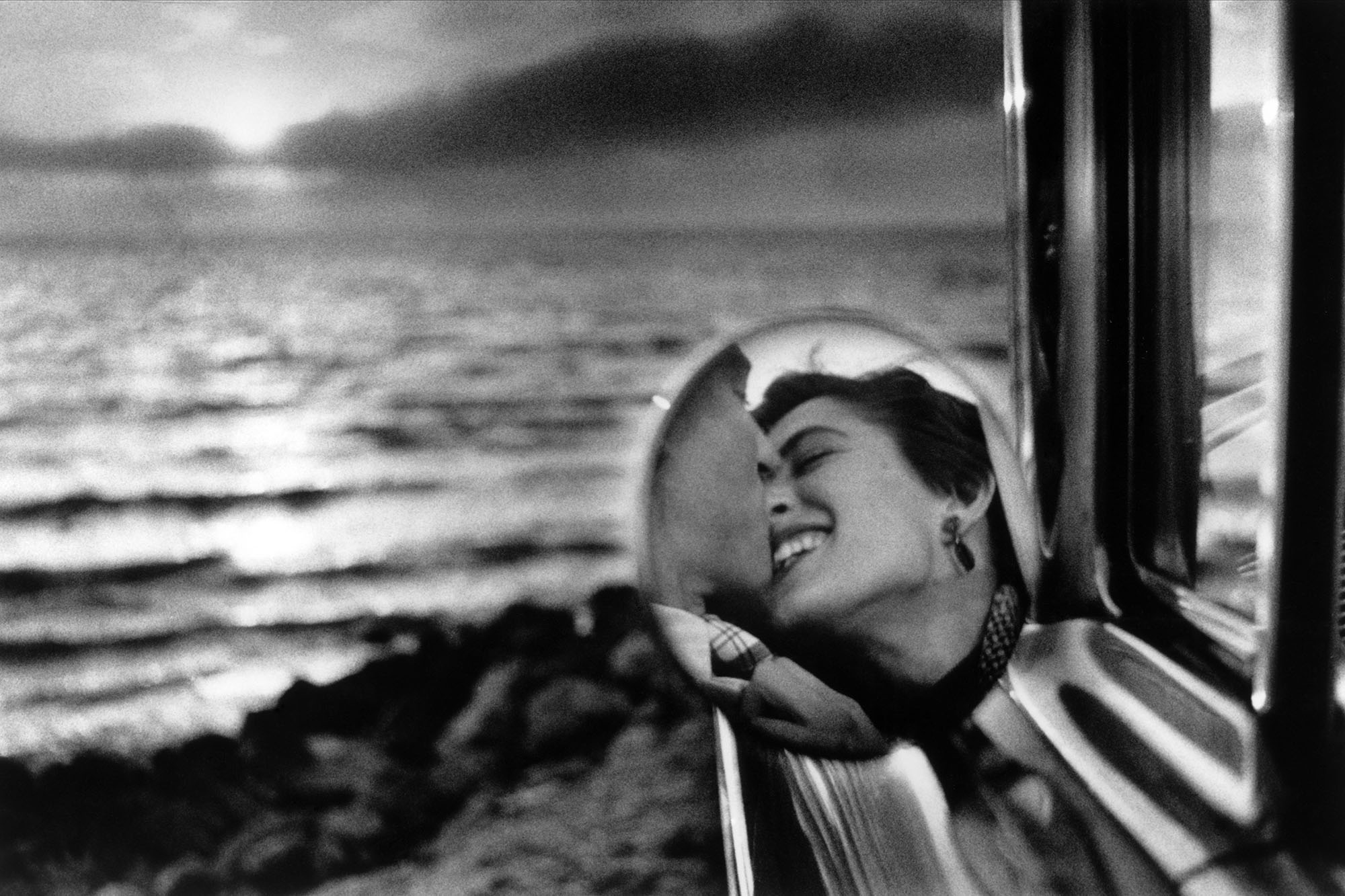 Couple kissing reflected in a car side mirror with ocean background, California, 1955 by Elliott Erwitt