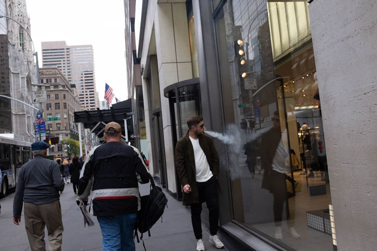 Street scene wide shot showing man smoking with reflection in store window