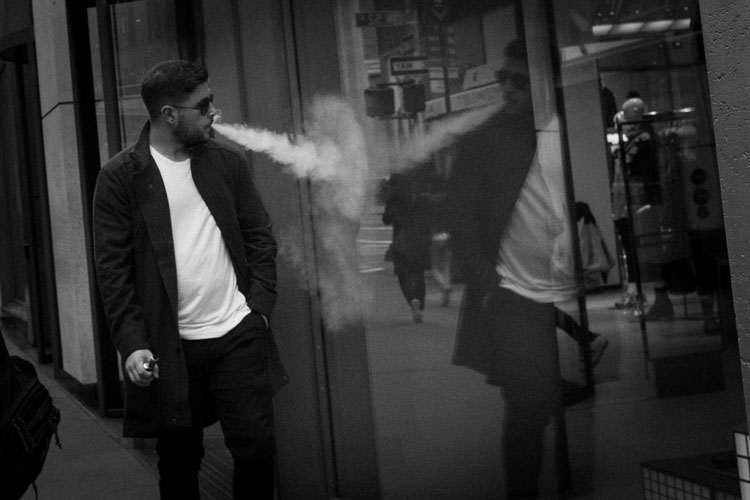 Man smoking edited to be cropped to focus on the subject and his reflection but doing so added a lot of noise