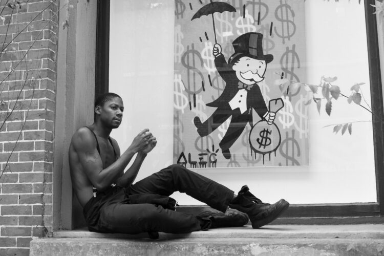 black and white photo of a shirtless man sitting in a window stoop as he rolls a cigarette