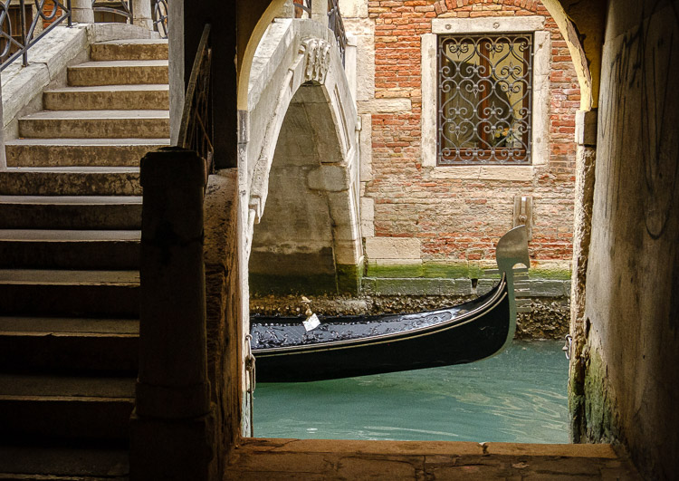 iconic photo of venice showing gondola passing underneath a bridge over the canal
