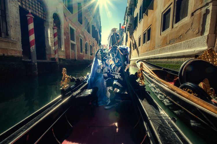 Costumed and masked characters in gondola on Venice canal with another sunflare