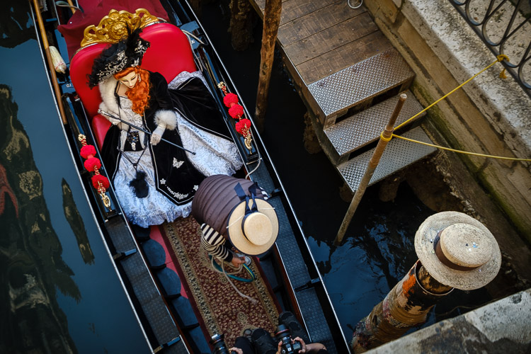 photo of passengers in a gondola as it passes below a bridge over the canal