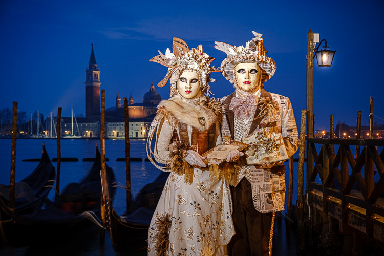 venice carnival costumes and masks at blue hour in front of gondolas with St. George's Cathedral in the distance