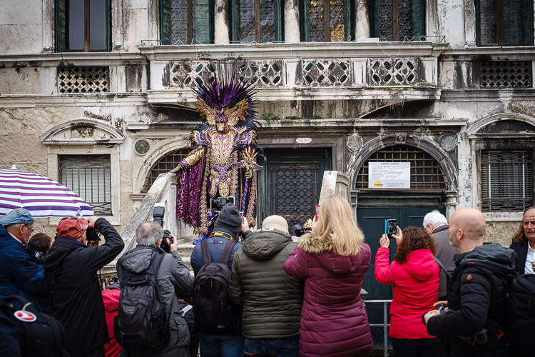 photographers competing for space to photograph a man in an amazing costume and mask on a bridge at venice carnival