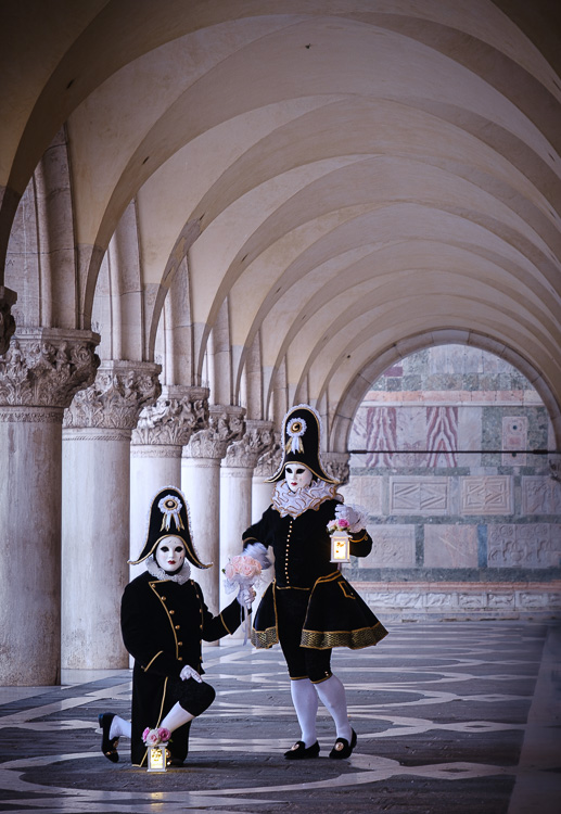 two masked and costumed characters pose under the archway beside the columns at Doge Palace