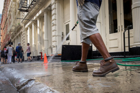man washes a sidewalk with a hose, photographed from the waist down, from a lower camera position