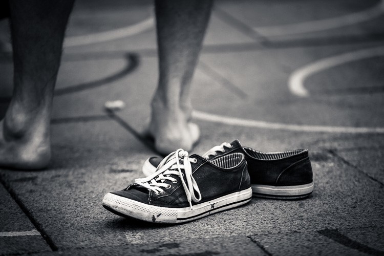 Bare feet on the sidewalk next to a pair of empty shoes
