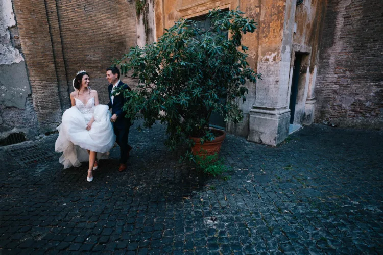 Outdoor photograph of a wedding couple next to a large plant with a stone wall behind them