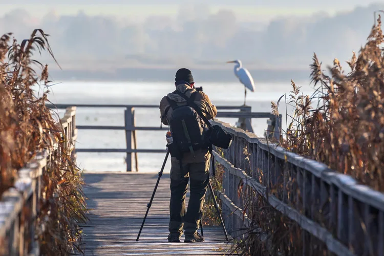 Photographer with a backpack camera bag and shoulder bag using his tripod to take a photo