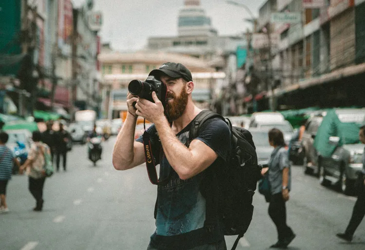 Photographer on the street wearing a backpack style camera bag while taking a picture